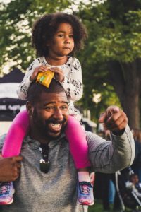 Smiling man holding his young daughter on his shoulders.